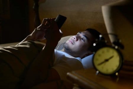 young-man-using-a-smartphone-in-his-bed-at-nightjpg