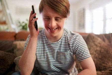 young-downs-syndrome-man-sitting-on-sofa-using